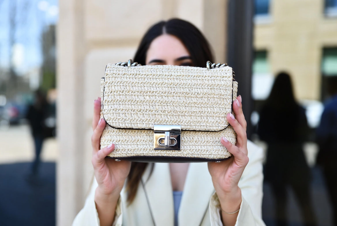 Person holding a textured handbag in front of their face with a blurred outdoor background