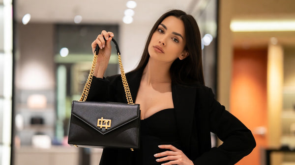 Woman holding a black handbag with gold accents in an indoor setting